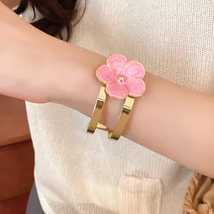 Vista detallada de un elegante brazalete de flores de esmalte rosa con acabado dorado en la muñeca.
