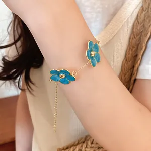 Vista detallada de una pulsera de cadena dorada con exquisitos colgantes de flores de esmalte azul