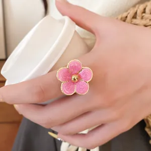Primer plano de un anillo de flor de esmalte rosa con bordes dorados y textura.