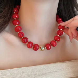 Detailansicht einer leuchtend roten Perlenkette mit goldenen Akzenten am Hals eines Models.