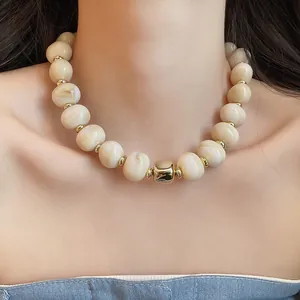 Detailansicht einer cremefarbenen Perlenkette mit Goldakzenten am Hals eines Models