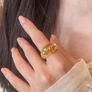 Detailansicht eines klobigen Bernstein-Harzrings mit bunten Kristall-Inlays an einer Hand