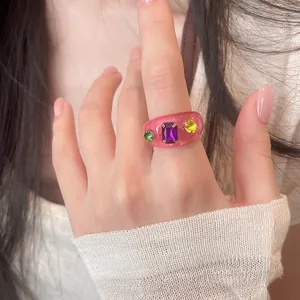 Detailansicht eines rosa Harzrings mit bunten Strasssteinen, getragen an einem Finger