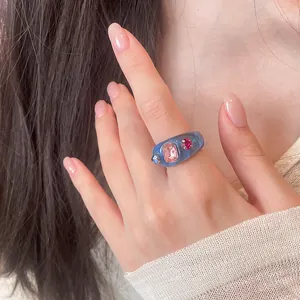 Exquisites Detail eines blauen Harzrings mit rosa und roten Strasssteinen an der Hand