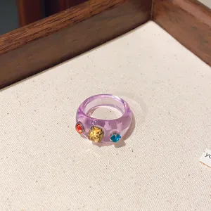 Detailansicht eines hellvioletten Harzrings mit bunten Edelsteinen in einem Tablett.