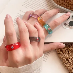 Nahaufnahme bunter Harzringe mit kleinen Kristallakzenten an einer Hand getragen