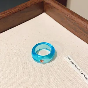 Detailaufnahme eines blauen transparenten Harzrings mit funkelndem rosa Strassstein