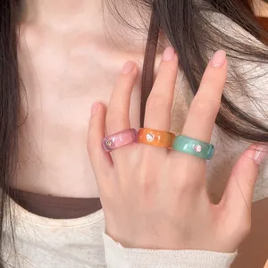Set aus farbenfrohen Harzringen mit funkelnden Strasssteinen an einer weiblichen Hand.