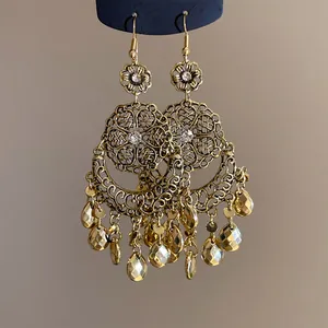 Dettaglio di orecchini vintage boho dorati con design floreale e pendenti a goccia sfaccettati