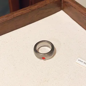 Detailansicht eines grauen, durchsichtigen Harzrings mit kleinem roten Kristall.
