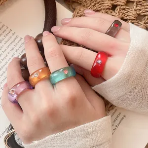 Nahaufnahme bunter Harzringe mit Strasssteinen an der Hand eines Models in Lifestyle-Szene