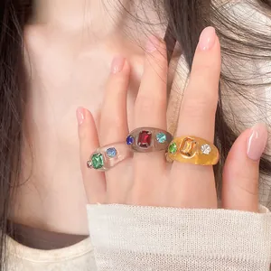 Nahaufnahme von drei stilvollen Harzringen mit bunten Strasssteinen an der Hand eines Models
