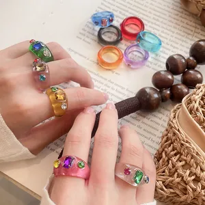 Hand mit mehreren bunten, klobigen Harzringen mit glitzernden Strasssteinen in Lifestyle-Szene