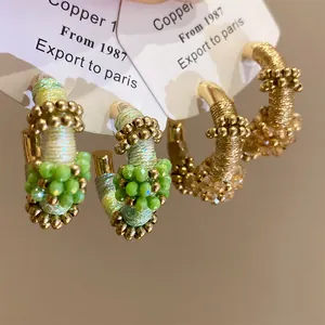 Primer plano de pendientes de aro en C envueltos en hilo de colores con cuentas finas.