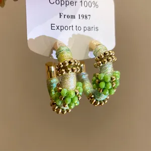 Primer plano de pendientes de aro étnicos con hilo multicolor y cuentas de cristal verde.
