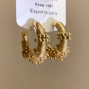 Vista detallada de pendientes de aro en forma de C envueltos en hilo dorado con cristales