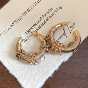 Primer plano de pendientes de aro dorados en forma de C estilo vintage con hilo y cuentas