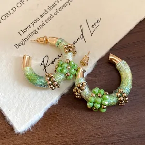 Detalle de pendientes de aro en C envueltos en seda de colores con cuentas de cristal