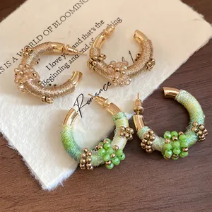 Primer plano detallado de pendientes étnicos en forma de C con hilo de colores y cuentas.