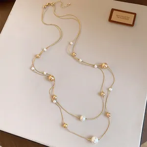 Elegante collar de doble capa con perlas blancas y cuentas doradas en fondo beige.