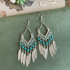 Detailweergave van vintage bohemien oorbellen met turquoise kralen en metalen veren.