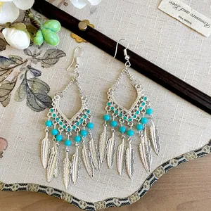 Vintage etnische oorbellen met turquoise kralen en zilveren veren kwastjes op stoffen ondergrond