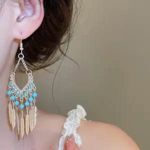 Detailopname van etnische veren oorbellen met turquoise kralen en zilveren afwerking