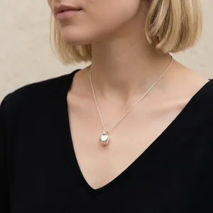 Gros plan d'un collier pendentif en argent minimaliste porté par un mannequin.