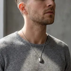 Vue détaillée d'un collier pendentif bouilloire en argent sur un pull gris.
