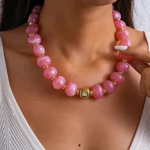 Dettaglio di una collana di perle acriliche marmorizzate rosa con elemento geometrico oro