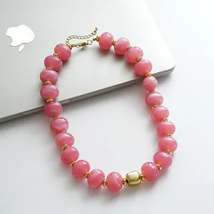Dettaglio di una collana retrò con perle acriliche venate rosa e accento geometrico oro.