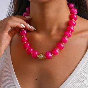 Dettaglio di una collana di perle acriliche rosa marmorizzate con ciondolo a cubo d'oro.