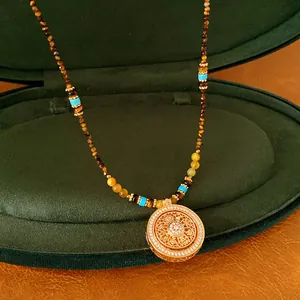 Gedetailleerd beeld van een 24k vergulde ketting met stenen kralen en een bloemenhanger.