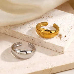 Ein Paar minimalistische, klobige, gewölbte offene Ringe in Gold und Silber auf Stein