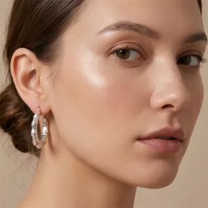 Close-up detail of a silver bamboo joint hoop earring worn by a model against beige background