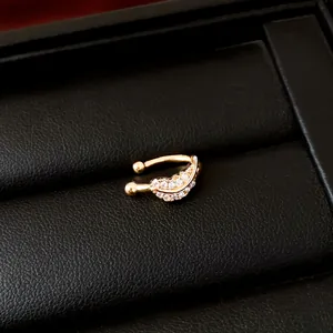 Detail view of a golden leaf-shaped ear cuff with sparkling zircons on black leather