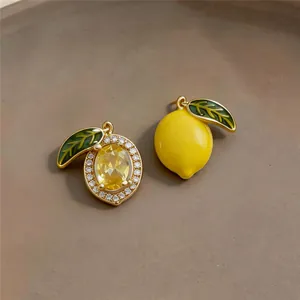 Close-up of asymmetric 14k gold plated lemon earrings with yellow crystal and enamel