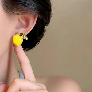 Close-up of dainty 14k gold-plated yellow lemon drop earrings worn on an earlobe.