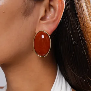 Close-up of vintage oval acrylic earrings with orange marbled pattern and gold trim