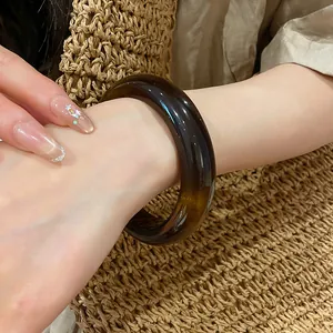 Gros plan d'un bracelet jonc en résine marron au poignet sur fond tissé