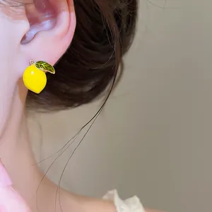 Close-up detail of a vibrant yellow lemon stud earring with a green leaf worn on the ear.