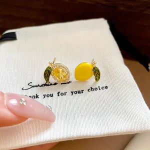 Close-up view of asymmetrical lemon earrings with yellow zircon and enamel details on white bag.