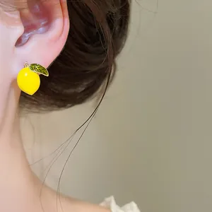 Close-up of a realistic yellow lemon enamel stud earring with a green leaf on an ear.