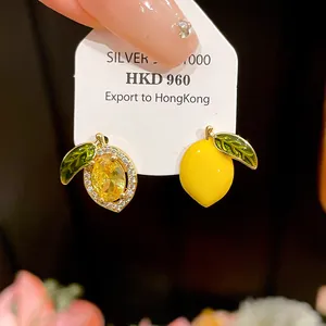 Macro detail of asymmetrical 14k gold plated lemon earrings with zircon and enamel