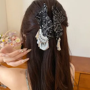 Detailweergave van zwarte paisley vlinder haarklem met zilveren kwastjes op lang haar