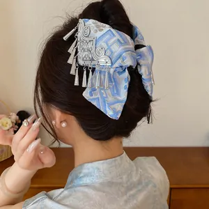Detailopname van een vintage blauwe stoffen haarklem met vlinderstrik en zilveren kwastjes.
