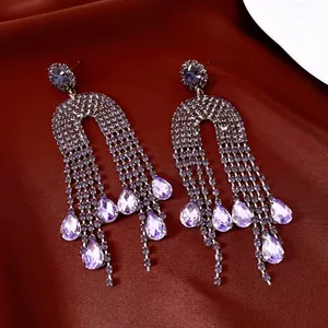 Detailed view of luxury purple teardrop crystal tassel earrings on deep red silk fabric.