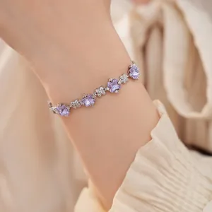 Detailansicht eines eleganten silbernen Blumenarmbands mit lila Zirkonsteinen am Handgelenk.