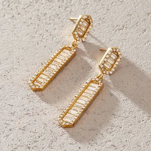 Dettaglio di eleganti orecchini pendenti in acciaio dorato con strass a baguette.
