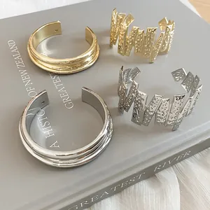 Detailed view of textured and smooth open metal cuff bracelets in gold and silver finishes
